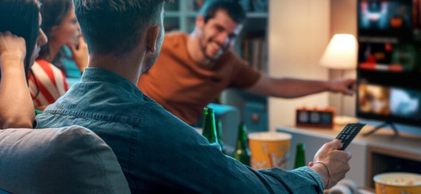 Four friends sitting on a living room couch and watching TV